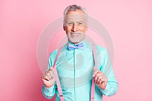 Photo portrait of handsome attractive senior man with toothy smile keeping suspenders bowtie shirt isolated on pink