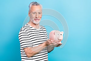 Photo portrait of handsome grandad hold piggy account bank economy dressed stylish striped clothes isolated on blue