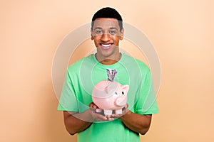 Photo portrait of handsome young male hands hold piggy banknotes money dressed stylish green outfit isolated on beige