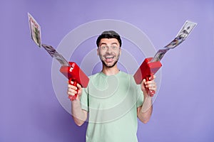 Photo portrait of handsome young man holding money gun cheerful crazy dressed stylish gray clothes isolated on purple