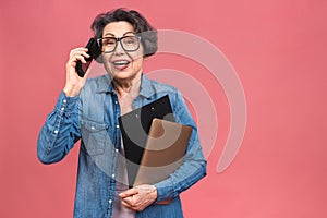 Photo portrait of happy senior mature aged woman holding mobile phone, grandmother wearing casual isolated on pink background.