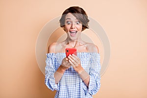 Photo portrait of impressed screaming girl holding phone in two hands isolated on pastel beige colored background