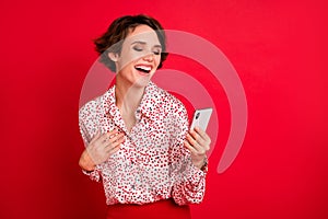 Photo portrait of laughing girl holding phone in one hand touching chest isolated on bright red colored background