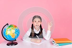 Photo portrait little girl with tails sitting at desk writing exam showing copyspace isolated pastel pink color