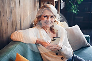 Photo portrait of lovely retired woman sit sofa hold device eshop dressed casual outfit cozy home interior living room