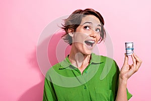 Photo portrait of lovely young lady hold money roll look excited empty space wear trendy green garment isolated on pink