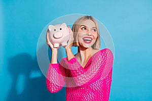 Photo portrait of lovely young lady hold piggy look empty space dressed stylish pink knitwear garment isolated on blue