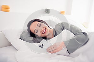 Photo portrait of lovely young lady lying bed hold gadget eshopping wear trendy gray sleepwear isolated on white bedroom