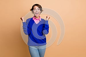 Photo portrait of lovely young lady raise fists excited celebrate lottery wear trendy blue garment isolated on beige