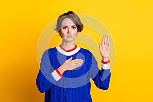 Photo portrait of lovely young lady raise palm touch chest swear wear trendy blue knitwear garment isolated on yellow