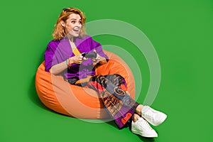 Photo portrait of lovely young lady sit beanbag have fun playstation dressed stylish violet clothes isolated on green