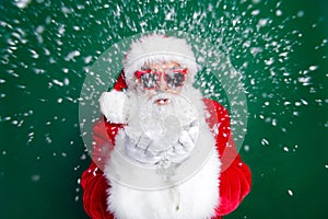 Photo portrait of mature pensioner man blowing snow camera wear trendy santa claus costume coat isolated on green color