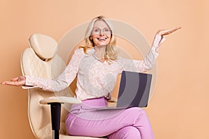 Photo portrait of nice retired female sit armchair hold netbook excited wear trendy formalwear isolated on beige color
