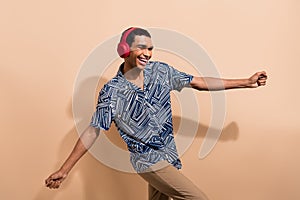 Photo portrait of nice young male dancing disco headphones wear trendy blue print garment isolated on beige color
