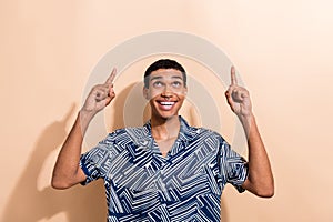 Photo portrait of nice young male look finger point up empty space wear trendy blue print garment isolated on beige