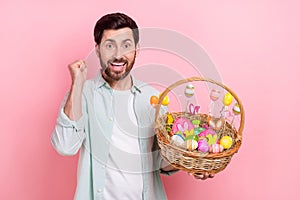 Photo portrait of nice young male raise fist excited hold basket easter eggs wear trendy blue garment isolated on pink