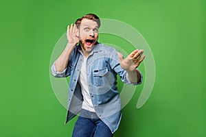 Photo portrait of overjoyed man listening gossip keeping hand near ear wearing casual clothes isolated bright green