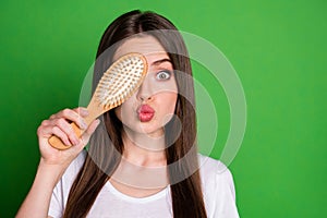 Photo portrait of pouting girl covering one eye with hairbrush isolated on vivid green colored background