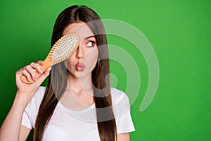 Photo portrait of pouting girl covering one eye with hairbrush looking at blank space isolated on vivid green colored