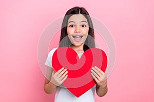 Photo portrait of pretty young child girl hold red heart figure shock dressed stylish white clothes isolated on pink