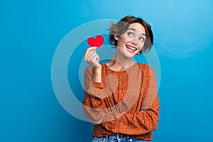 Photo portrait of pretty young girl hold little red heart look empty space wear trendy brown outfit isolated on blue