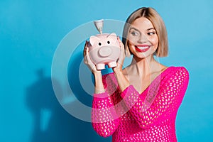 Photo portrait of pretty young girl hold look interested money piggy wear trendy pink knitted outfit isolated on blue