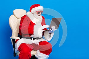 Photo portrait of retired old man sit armchair work remotely dressed stylish santa claus costume coat isolated on blue