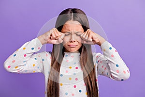 Photo portrait of sad crying child wiping tears with hands fists isolated on bright purple colored background