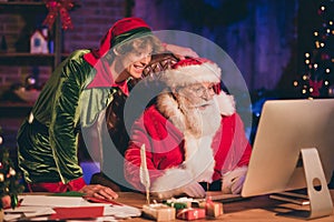 Photo portrait of santa claus and elf browsing internet on desktop