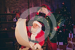 Photo portrait of santa claus and elf reading nice and naughty list together