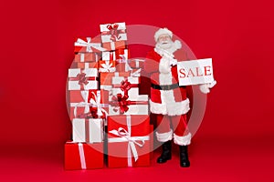 Photo portrait of santa claus holding sale paper card next to big stack of presents wearing costume glasses isolated on