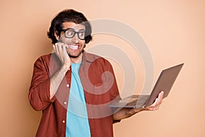 Photo portrait of scared man biting nails holding laptop in hand isolated on pastel beige colored background