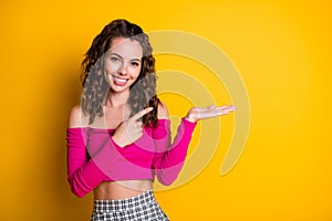 Photo portrait of schoolgirl pointing finger at your product blank space holding hand palm wearing pink top checkered