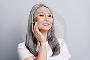 Photo portrait of senior woman with grey hair touching cheek wearing white t-shirt smiling isolated on grey color