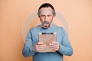 Photo portrait of shocked businessman reading fake news in internet keeping tablet isolated on pastel beige color
