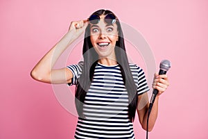 Photo portrait of shocked woman lifting up glasses holding microphone in one hand isolated on pastel pink colored