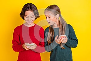 Photo portrait two children keeping mobile phones playing games isolated vivid yellow color background