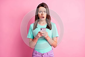 Photo portrait of upset woman holding phone in two hands isolated on pastel pink colored background