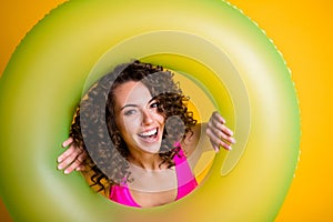 Photo portrait of woman looking through inflatable green ring wearing pink swim wear  on bright yellow colored