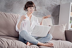 Photo portrait woman wearing white shirt using computer drinking coffee at home on couch talking on web camera