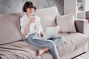 Photo portrait woman wearing white shirt using computer typing message drinking coffee at home on couch
