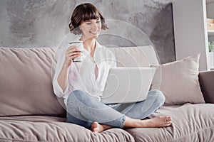 Photo portrait woman wearing white shirt using computer watching movie relaxing drinking coffee at home on couch