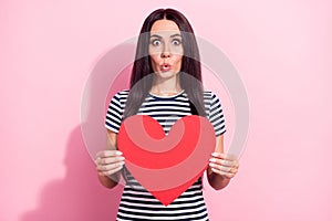 Photo portrait of young girl in striped t-shirt surprised keeping heart card on date isolated on pastel pink color