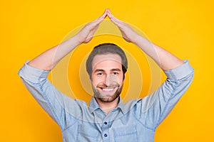 Photo portrait of young guy smiling keeping hands over head safety insurance isolated on bright yellow color background