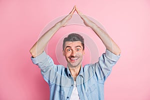 Photo portrait of young man keeping hands over head showing roof insurance safety smiling isolated pastel pink color