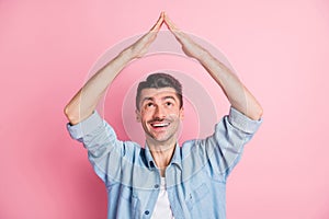 Photo portrait of young man keeping hands over head showing roof moving to new house isolated pastel pink color