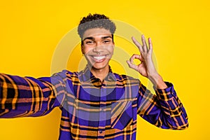 Photo portrait of young man smiling cheerful happy showing okay sign taking selfie isolated vibrant yellow color