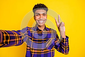 Photo portrait of young man smiling cheerful happy showing v-sign two fingers taking selfie isolated bright yellow color