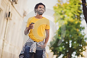 Photo portrait of young man smiling enjoying street walk in sunny day along green streets drinking hot beverage