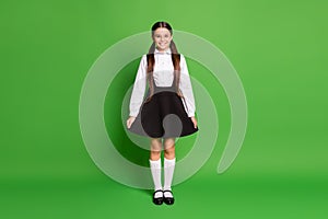 Photo portrait of young schoolgirl holding demonstrating her skirt isolated on vivid green colored background